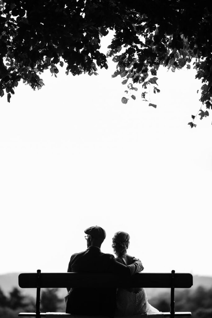 couple sitting on bench under tree grayscale photography